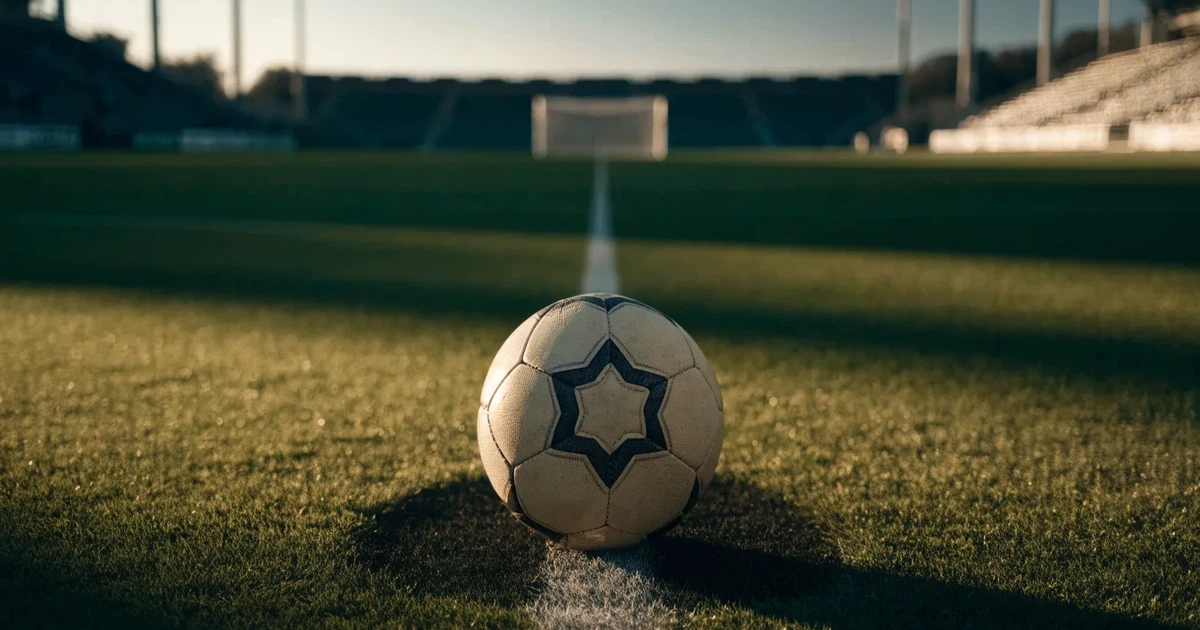 Uma bola de futebol no ponto central de um relvado, à luz da manhã